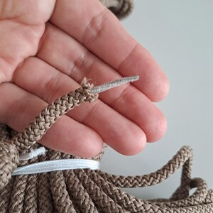 May include: Close-up of a brown braided rope with a frayed end. The rope is held in a hand, and the frayed end is visible.