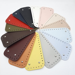 May include: A collection of colorful, leather-like bag bases in various shades, including red, blue, and yellow. Each base is a semi-circular shape with pre-punched holes for easy sewing and a metal stud in the center.