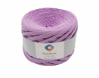 May include: A skein of lavender-colored t-shirt yarn, made from 100% cotton. The yarn is wound around a cardboard tube with a label that reads "Rainbow T-shirt yarn 100% cotton".
