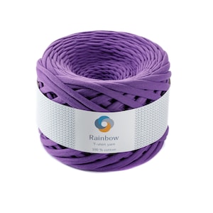 May include: A ball of purple Rainbow T-shirt yarn, 100% cotton, with a white label. The yarn is tightly wound, showing the texture of the fabric. The label features a colorful logo and the words "Rainbow T-shirt yarn".