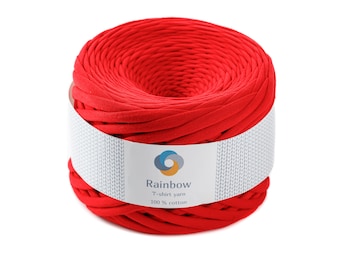 May include: A vibrant red T-shirt yarn, tightly wound into a cylindrical shape. A white label wraps around the yarn, displaying the brand name "Rainbow" and the text "T-shirt yarn 100% cotton". The yarn is a solid, bright red color.