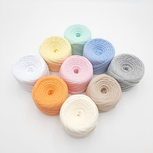 Op de afbeelding: Assortiment van acht kleurrijke garenbollen in verschillende tinten blauw, roze, geel, oranje, beige en grijs. Het garen is gemaakt van zachte katoenen stof en is perfect voor knutselprojecten.