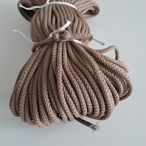 May include: A close-up of a tightly wound bundle of brown cotton rope. The rope is thick and has a natural, rustic look.