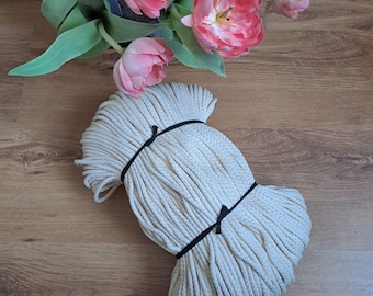 Puede incluir: Un fardo de cuerda blanquecina, atado con cintas negras, descansa sobre una superficie de madera. Tulipanes rosas y hojas verdes se disponen en el fondo. La cuerda parece estar hecha de un material tejido.