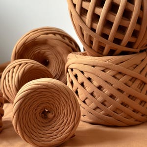 May include: A collection of brown yarn balls made from recycled t-shirts. The yarn is thick and textured, perfect for crocheting or knitting.