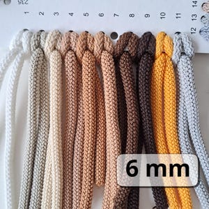Op de afbeelding: Een kleurenkaart met 11 verschillende kleuren van 6 mm dik koord. De kleuren variëren van lichtgrijs tot donkerbruin en geel.
