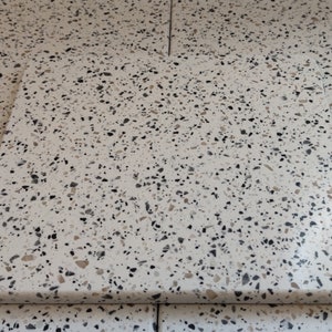 May include: A white rectangular chopping board with a speckled pattern of black, grey, and tan flecks. The board has rounded corners and a smooth surface, suitable for food preparation.