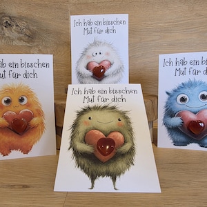 May include: Four white greeting cards featuring fluffy, colorful monsters holding red hearts. Each card displays the German text 'Ich hab ein bisschen Mut für dich' above a central illustration of a yellow, white, green, or blue creature.