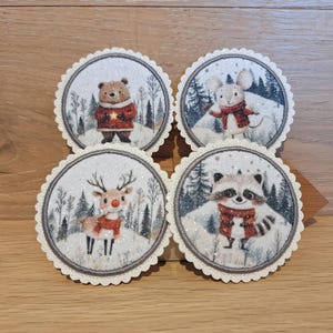 Könnte beinhalten: Vier runde Untersetzer mit gewellten Rändern, die jeweils ein anderes Wintertier zeigen: einen Bären, eine Maus, ein Reh und einen Waschbären. Die Tiere sind in Winterkleidung gekleidet und vor einem verschneiten Waldhintergrund platziert. Die Untersetzer haben einen Durchmesser von etwa 10 cm.