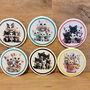 Könnte beinhalten: Sechs runde Untersetzer mit bunten Rändern, die verschiedene Gruppen von Comic-Katzen zeigen. Jeder Untersetzer hat einen anderen Farbrand: blau, rosa, gelb, schwarz, weiß und türkis. Die Katzen sind in verschiedenen Posen dargestellt, einige sitzen, einige stehen und einige schauen den Betrachter an. Die Untersetzer sind perfekt, um jedem Zuhause einen Hauch von Verspieltheit zu verleihen.