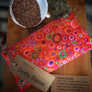 May include: Handmade lavender heat pad with a colourful, orange, pink and green circle pattern. The pad is made with 100% cotton and filled with brown flax seeds. The text on the tag reads "Handmade by Dotty Daisies".