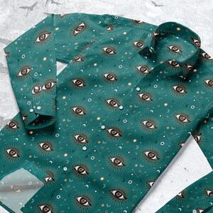Op de afbeelding: Een tealblauw overhemd met knopen en een herhalend patroon van gouden ogen met zonnestralen en halve manen.