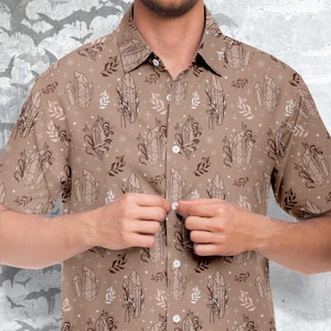 Puede incluir: Una camisa de manga corta de color marrón con botones y un patrón de cristales blancos y pequeñas hojas marrones.