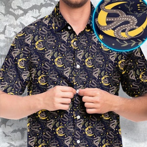 May include: A navy blue short-sleeved button-down shirt with a repeating pattern of snakes and moons. The snakes are yellow and brown, and the moons are yellow. The shirt has a button-up collar and a button closure.