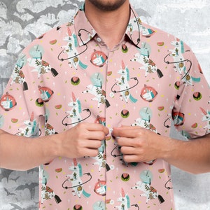 May include: A pink short-sleeved button-down shirt with a repeating pattern of unicorns wearing astronaut helmets and holding watermelon slices. The unicorns are surrounded by stars and planets.