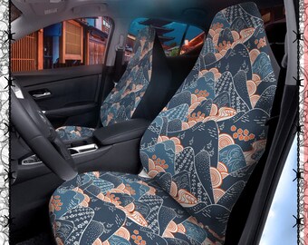 May include: A pair of car seat covers with a blue and white mountain and wave pattern. The covers have a modern, abstract design with orange accents.