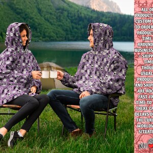 May include: Two people wearing purple hooded sweatshirts with a white and black skull pattern are sitting on chairs outdoors. The sweatshirts have a hood and a pouch pocket. The text on the right side of the image reads: "ALL OUR PRODUCTS ARE CUSTOM MADE TO ORDER, AND PRODUCTION TIME IS AROUND 2-8 BUSINESS DAYS + SHIPPING TIME. THOUGH USUALLY PRODUCTION AND SHIPMENT ARE ROCKET FAST, FROM TIME TO TIME THERE CAN BE DELAYS DUE TO THE CURRENT WORLDWIDE SITUATION. NEO"