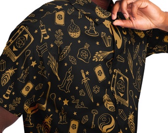 May include: Black button-up shirt featuring a gold pattern of occult symbols, such as books, candles, crystals, and tarot cards. The shirt has short sleeves and a classic collar. The design has a mystical theme.