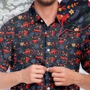 May include: Dark navy button-up shirt with a repeating pattern of red monkeys, yellow flowers, and green foliage. The shirt has a classic collar and white buttons. The design is detailed and vibrant, creating a tropical or jungle theme.