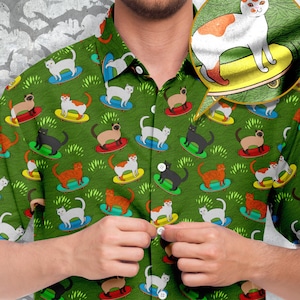 May include: A green button-down shirt with a pattern of cats riding skateboards. The cats are in various colors and poses, and the skateboards are all yellow with black wheels. The shirt has a button-up collar and short sleeves.