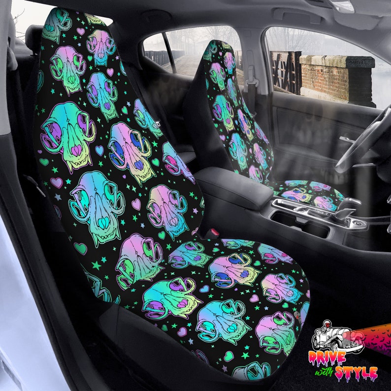 May include: A pair of black car seat covers with a colorful skull and heart pattern. The skulls are iridescent and have a rainbow gradient. The hearts are pink, green, and blue. The background is black with stars.