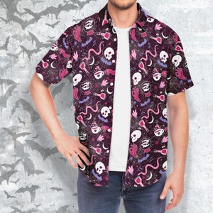 Puede incluir: Camisa de manga corta con fondo morado oscuro y un patr&oacute;n repetido de calaveras blancas, botellas de pociones, manos, murci&eacute;lagos y telara&ntilde;as. La camisa est&aacute; abierta, revelando una camiseta blanca.