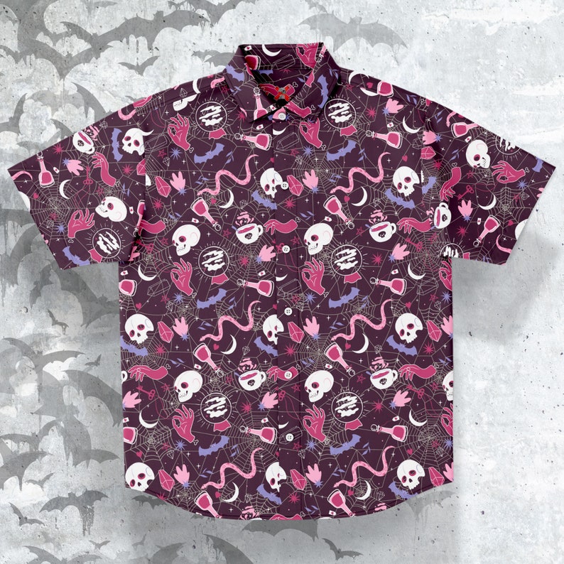 Puede incluir: Camisa de manga corta con botones, con un fondo morado oscuro y un patr&oacute;n repetido de calaveras blancas, manos rosas, botellas de pociones y telara&ntilde;as. La camisa tiene un cuello cl&aacute;sico y una parte delantera abotonada. El dise&ntilde;o es de tem&aacute;tica de Halloween.