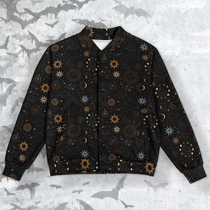 Puede incluir: Una chaqueta bomber negra con un patrón celestial dorado con soles, lunas y estrellas. La chaqueta tiene una cremallera y puños y cintura de canalé.