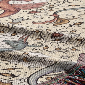 May include: A cream-colored woven throw blanket with a floral pattern in shades of brown, pink, and blue. The blanket has a fringe border.