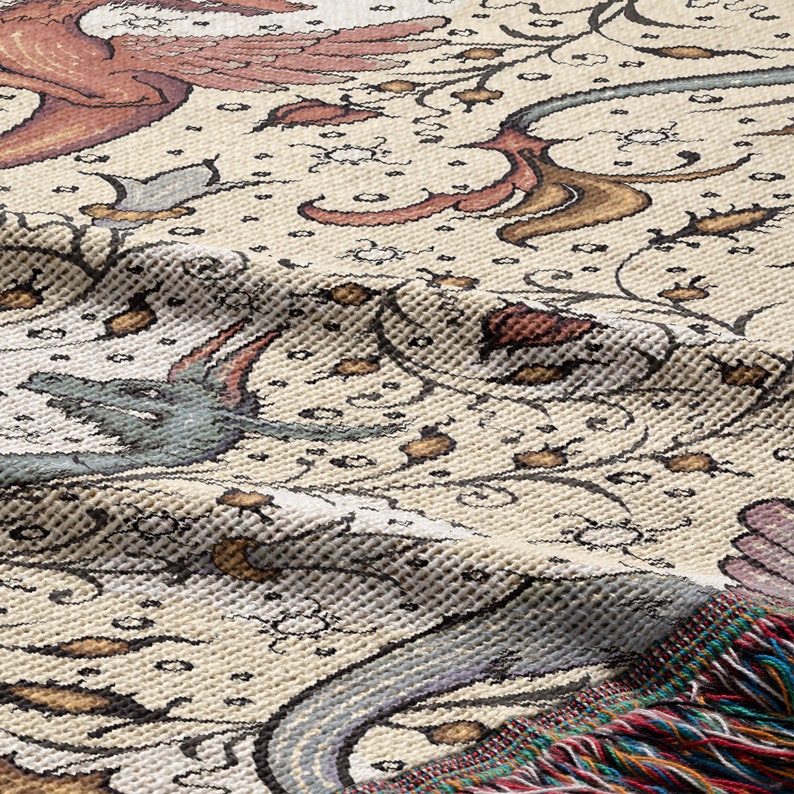 May include: A cream-colored woven throw blanket with a floral pattern in shades of brown, pink, and blue. The blanket has a fringe border.