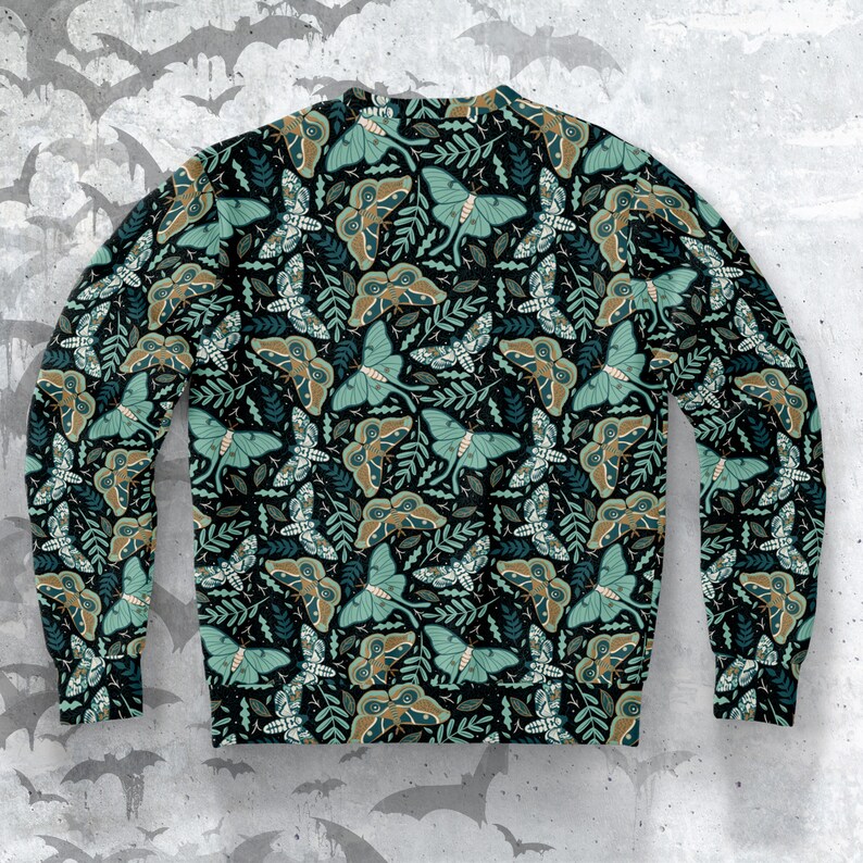 May include: A black sweatshirt with a repeating pattern of green and brown moths on a dark background. The moths have large, intricate wings and are surrounded by leaves and vines.