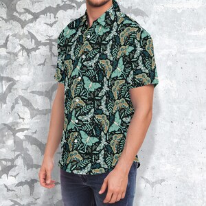 Puede incluir: Una camisa de manga corta con botones, fondo oscuro y un patr&oacute;n repetido de polillas verdes y marrones y hojas.