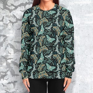 May include: A black sweatshirt with a green and brown moth pattern. The moths are arranged in a repeating pattern on a dark background.