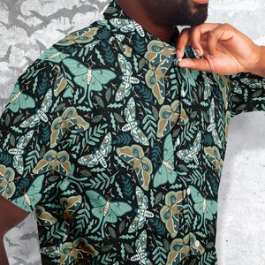 Puede incluir: Una camisa negra de botones con un patr&oacute;n repetido de polillas verdes y marrones sobre un fondo verde oscuro.