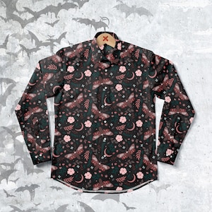 May include: A long-sleeved button-down shirt with a dark background and a repeating pattern of pink flowers, crescent moons, and brown moths.