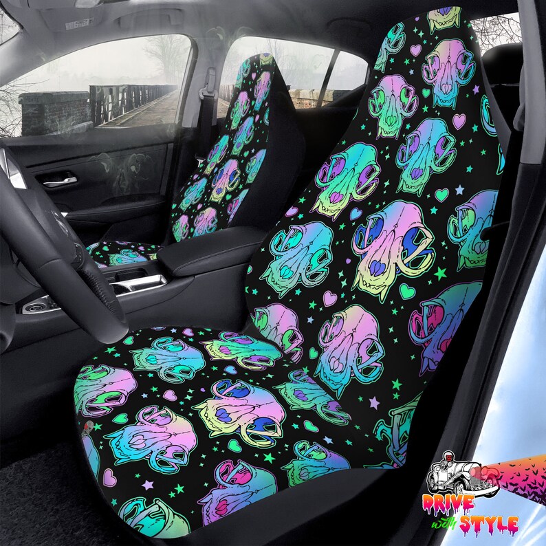 May include: A pair of black car seat covers with a colorful skull and heart pattern. The skulls are iridescent and have a rainbow color scheme. The background is black with white stars and pink hearts.