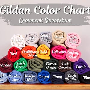 Peut inclure: Un nuancier pour les sweatshirts Gildan. Le tableau pr&eacute;sente une vari&eacute;t&eacute; d'&eacute;chantillons de tissu roul&eacute;s dans des couleurs telles que le blanc, le rouge, le marine et le noir. Des &eacute;tiquettes de texte identifient chaque couleur.