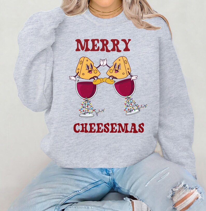 May include: Gray sweatshirt with a Christmas-themed design featuring two cartoon cheese wedges holding glasses of wine. The text reads "Merry Cheesemas".
