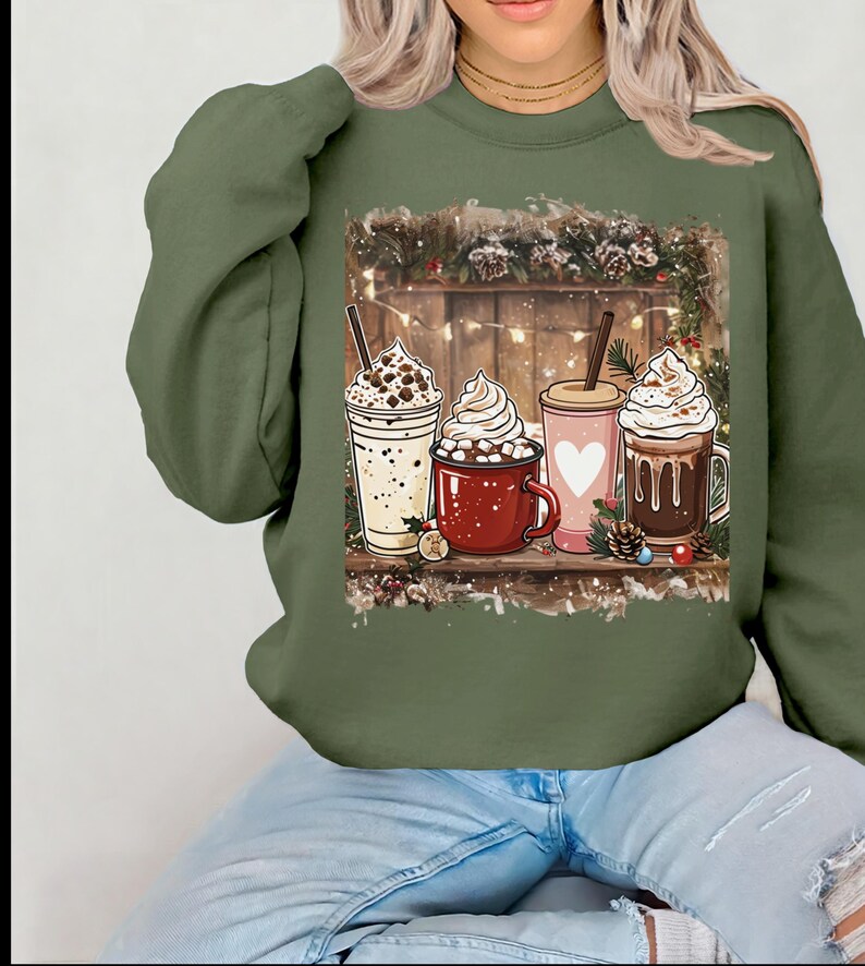 Peut inclure: Un sweat-shirt vert olive avec un motif de quatre boissons festives : un milk-shake, une tasse de chocolat chaud, une tasse rose avec un c&oelig;ur et une tasse de caf&eacute;. Les boissons sont d&eacute;cor&eacute;es de cr&egrave;me fouett&eacute;e et d'autres garnitures.