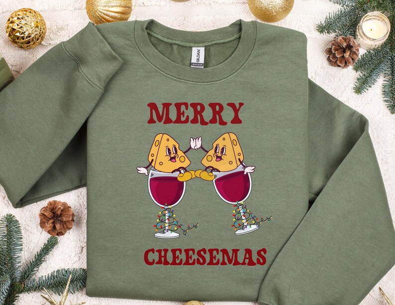 May include: Green sweatshirt with a red graphic of two cheese wedges holding glasses of wine. The text "Merry Cheesemas" is printed below the graphic.