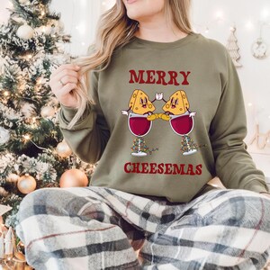 May include: A green sweatshirt with the text "Merry Cheesemas" and a graphic of two cheese wedges holding glasses of wine.