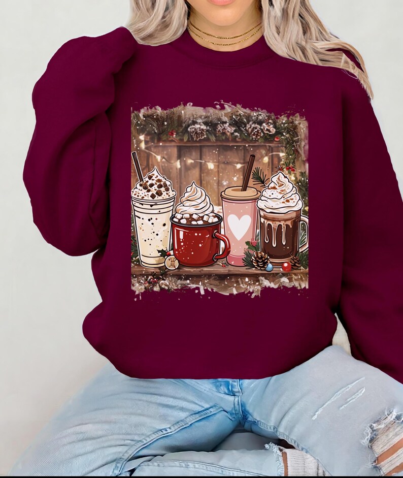 Peut inclure: Un sweat-shirt bordeaux avec un motif de quatre boissons chaudes festives &agrave; la cr&egrave;me fouett&eacute;e. Les boissons sont dans diverses tasses et mugs, sur fond de bois avec des d&eacute;corations de No&euml;l. Le sweat-shirt est port&eacute; par une personne en jean bleu.