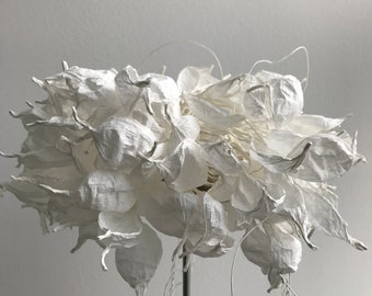 May include: A white paper flower sculpture with delicate, flowing tendrils. The sculpture is made of many individual paper flowers, each with a unique shape and texture. The flowers are arranged in a cluster, creating a sense of movement and lightness.