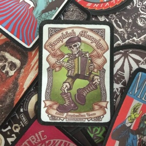 May include: A white patch with black trim features a cartoon skeleton playing an accordion. The skeleton is wearing a green hat and green trousers. The text on the patch reads "Dropkick Murphys" and "2012 Australian Tour".