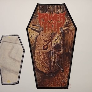 Può includere: Un cerotto a forma di bara in bianco e nero con un'immagine marrone e rossa di un ceppo d'albero con una pipa che sporge. Il testo "POWER TRIP" è scritto in rosso sul cerotto.