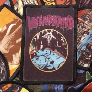 May include: A black and purple embroidered patch with the text "WINDHAND" in white lettering. The patch features a circular design with a pentagram and a figure with horns and a crown.