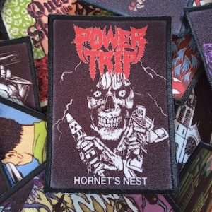 May include: Black and red embroidered patch with a skull holding a syringe and a bag of money. The text "POWER TRIP" is in red and the text "HORNET'S NEST" is in white.