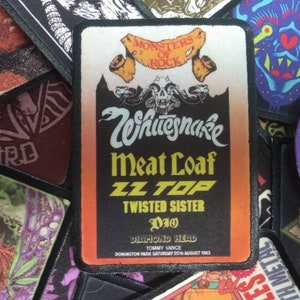Peut inclure: Un patch noir et orange avec le texte "Monsters of Rock" et les noms de groupes dont Whitesnake, Meat Loaf, ZZ Top, Twisted Sister et Dio. Le patch comprend également le texte "Diamond Head", "Tommy Vance" et "Donington Park Samedi 20 août 1983".