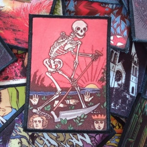 May include: Rectangular patch featuring a skeletal figure with a scythe against a red background with a setting sun. The patch is surrounded by other patches with various designs, including a church and other illustrations.