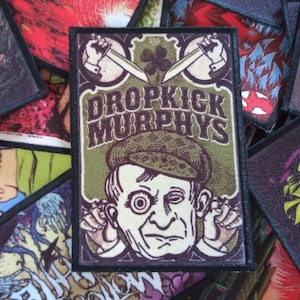 May include: A green and brown embroidered patch with the text "Dropkick Murphys" and a cartoon image of a man with a green hat and a single eye.